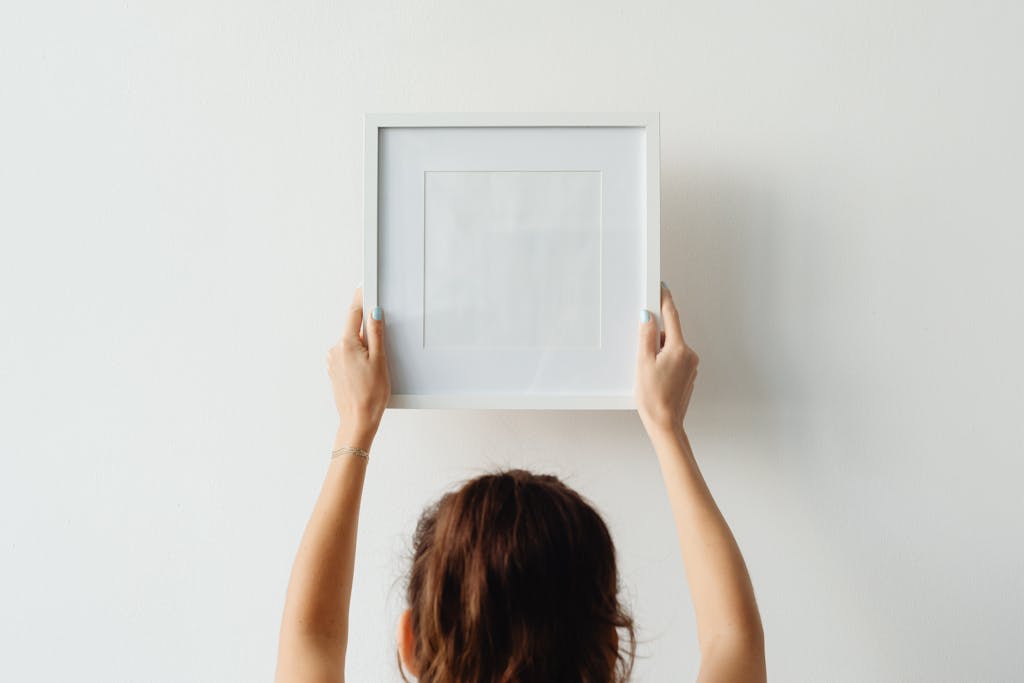 A woman hangs an empty frame on a white wall with copy space.